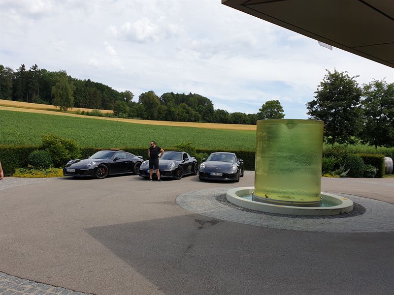 Three Porsche 911s parked at a luxury Bavarian hotel with green fountain